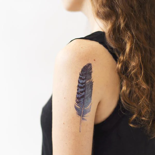 Feather with blue and black spots inked on a woman's shoulder