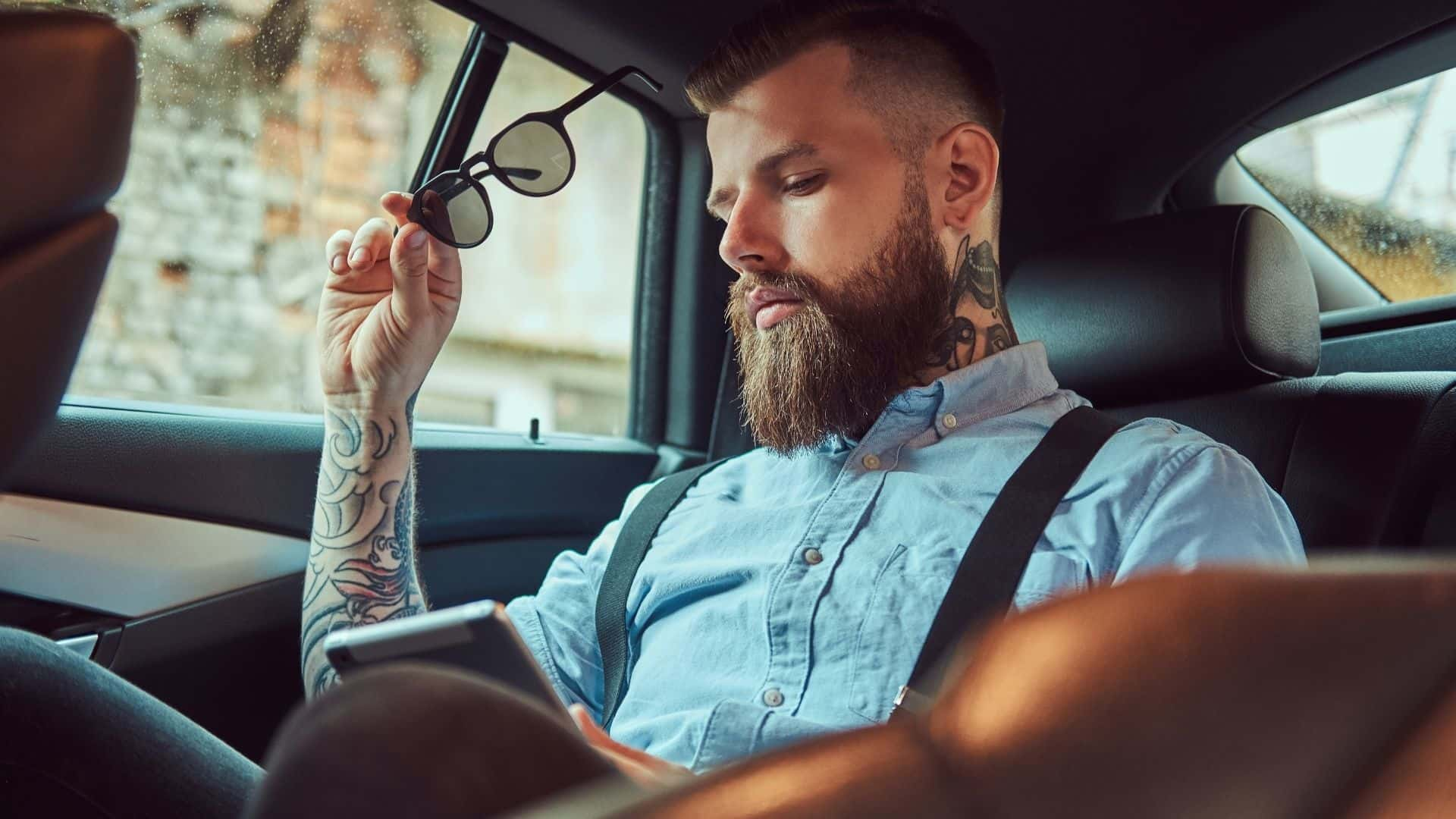 A tattooed guy with beard sitting in a car