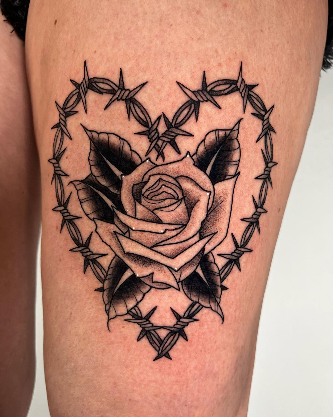 A tattoo of barbed wire in the form of a heart with a rose inside