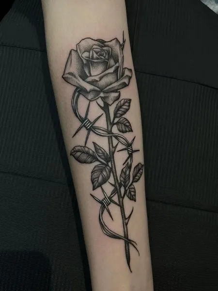 A rose intertwined with barbed wire inked on a forearm