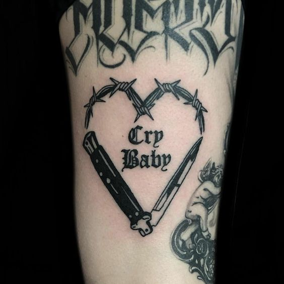 The tattoo of barbed wire combined with a crybaby caption and a knife