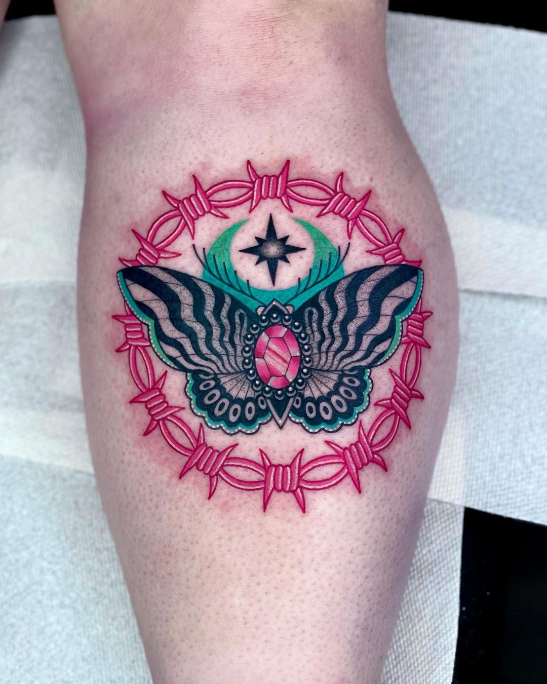 A tattoo of pink barbed wire in the form of a circle with a colorful butterfly inside