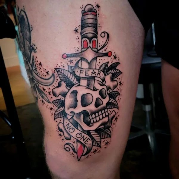 The "Fear None" tattoo on the thigh is almost ideal because it is in a relatively noticeable location, it is not painful to ink, and it may be as little or as large as desired, with various details as seen in the image.