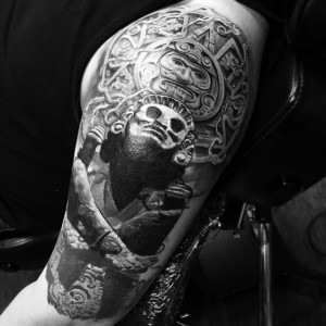 Black and white image of a man with an Aztec skull tattoo