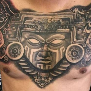 Full-chest tattoo of an Aztec mask design with tribal symbols