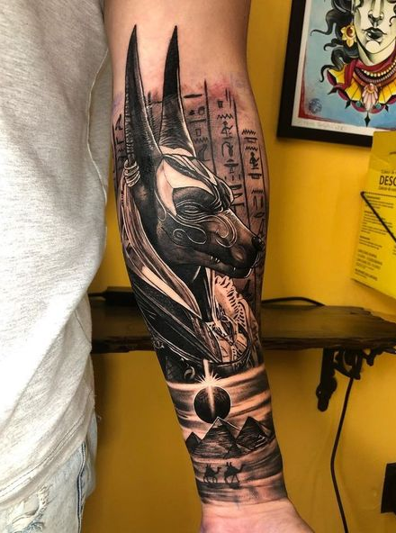 Anubis with pyramids, sun, and runes inked on the arm
