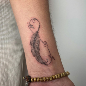 A wrist tattoo of a feather with infinity and the letter